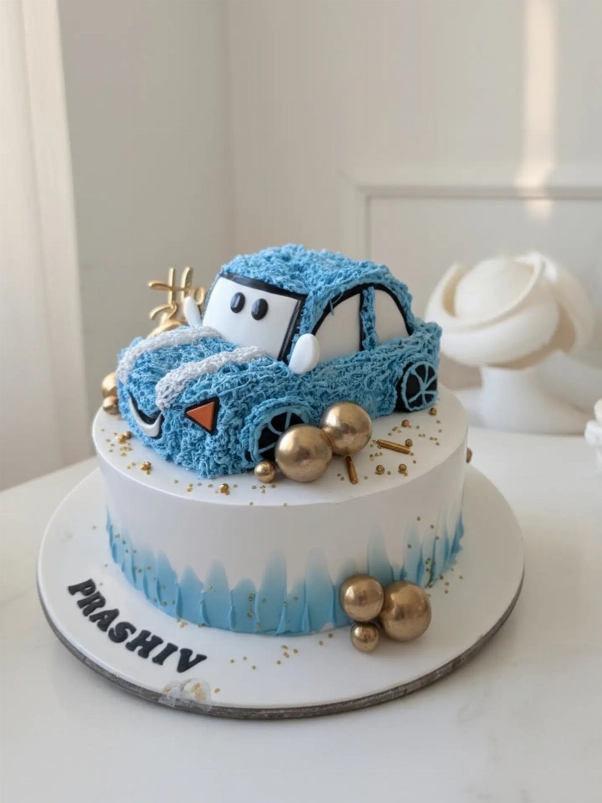 Blue car cake with white frosting and gold decorations on a white board.