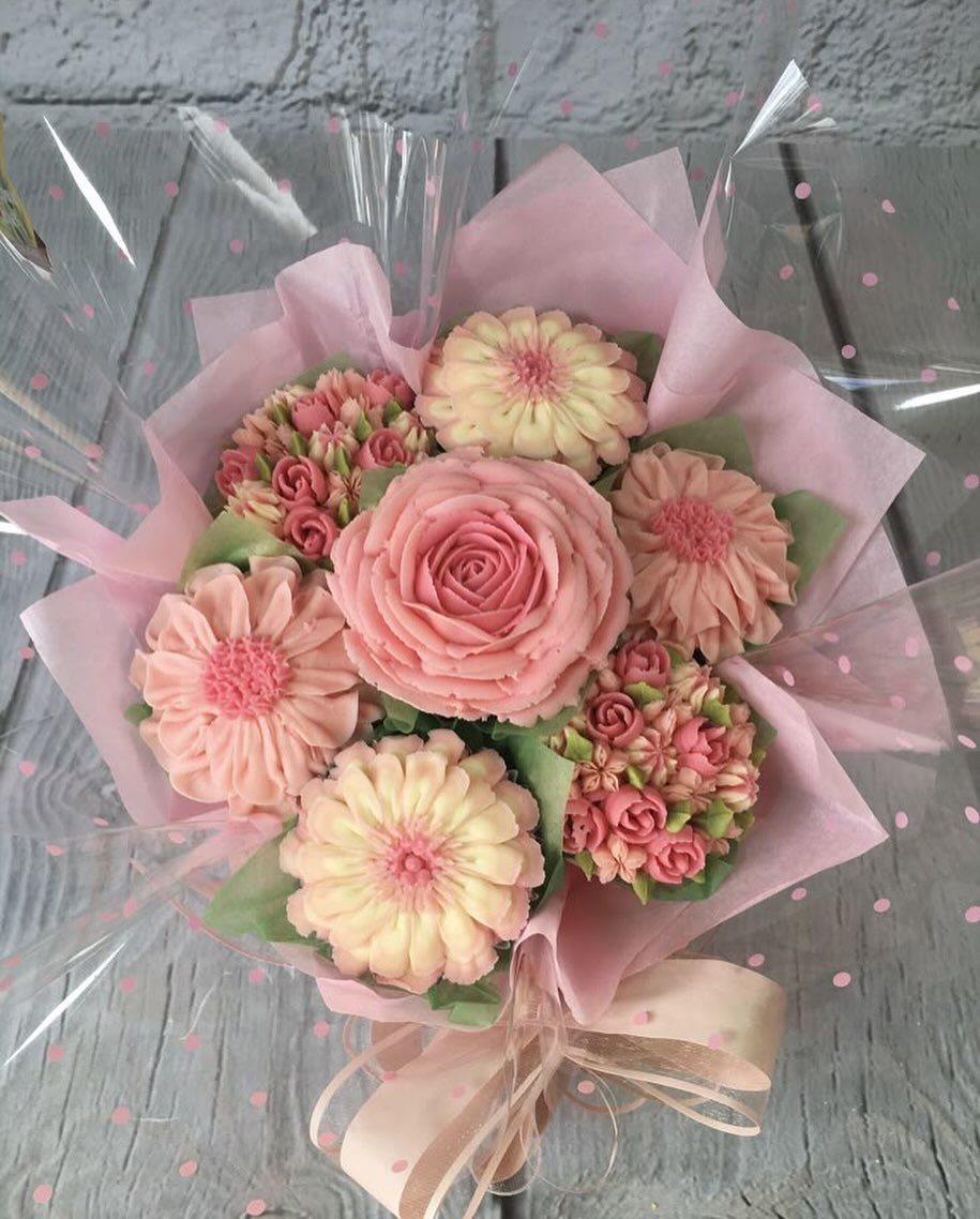 Cupcake bouquet with pink and cream frosting flowers wrapped in pink paper and cellophane.