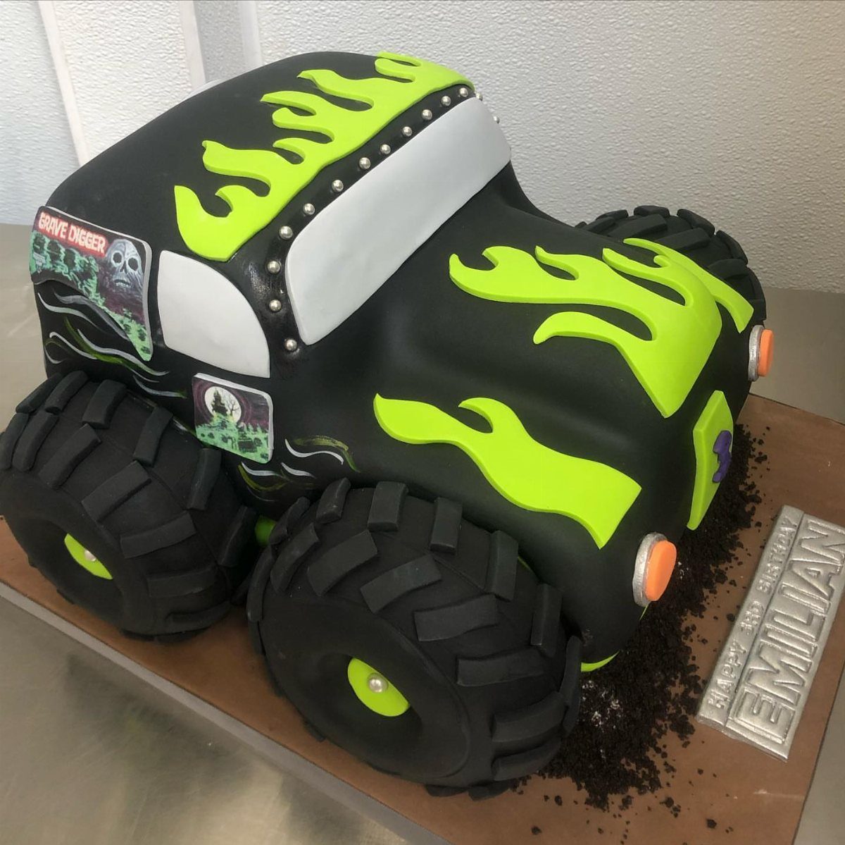 3D monster truck cake with black fondant, lime green flames, and large edible tires.